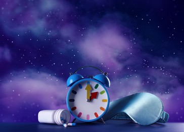 Alarm clock, soporific pills and sleeping mask on blue wooden table against night sky with stars. Insomnia