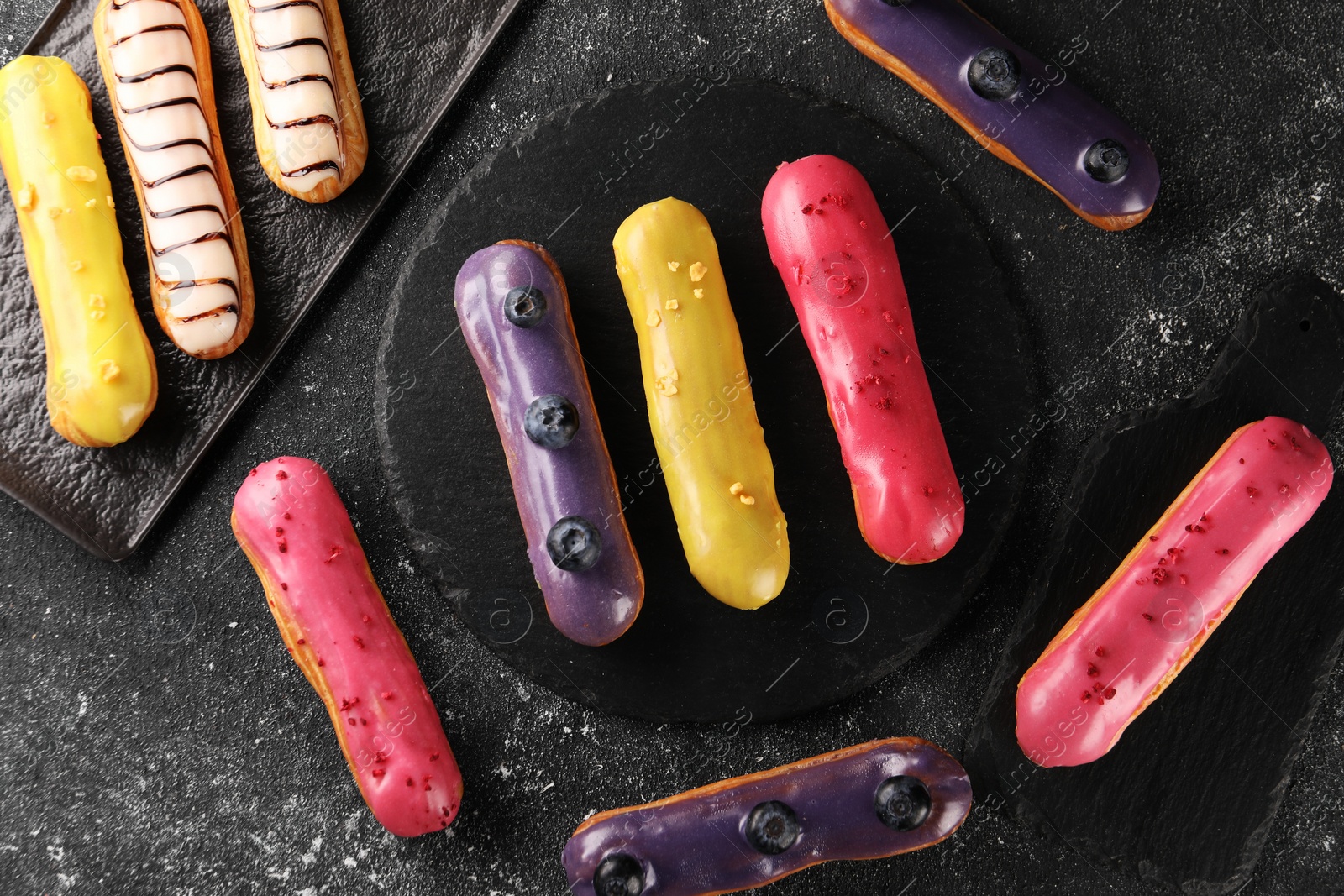 Photo of Different tasty glazed eclairs on dark textured table, flat lay