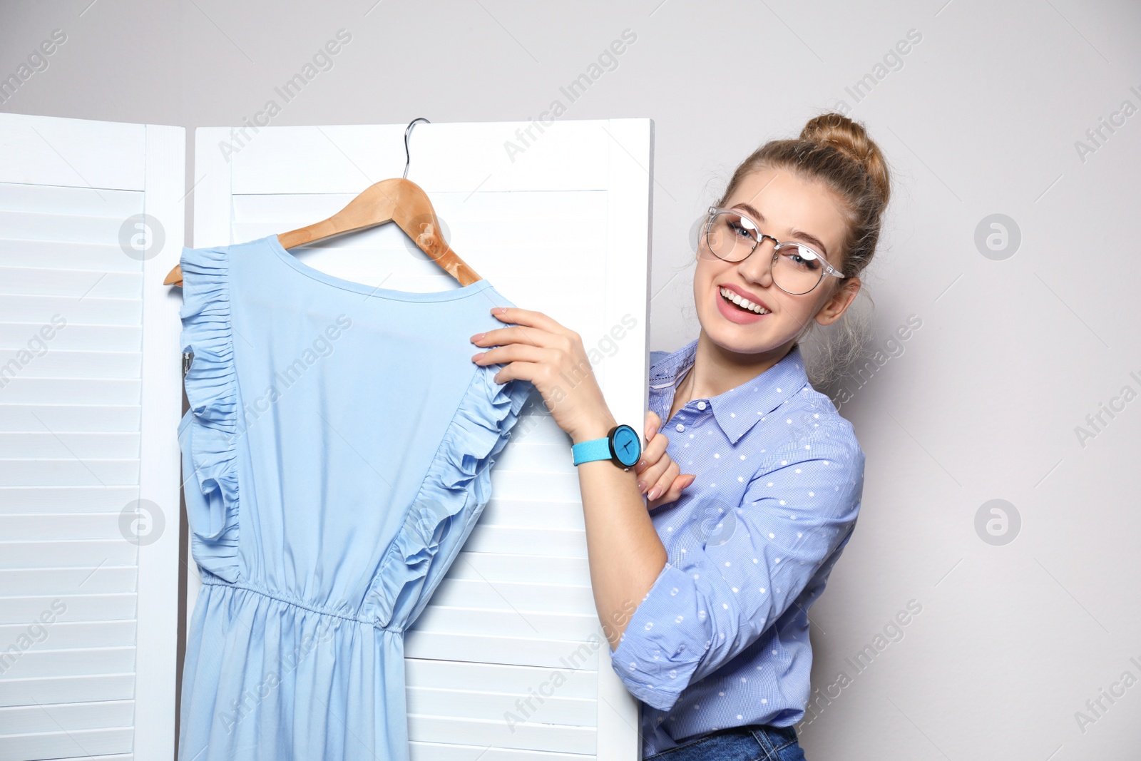 Photo of Young woman with clothes on hanger near folding screen against light background. Dressing room