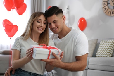 Photo of Man presenting gift to his girlfriend in room decorated with heart shaped balloons. Valentine's day celebration