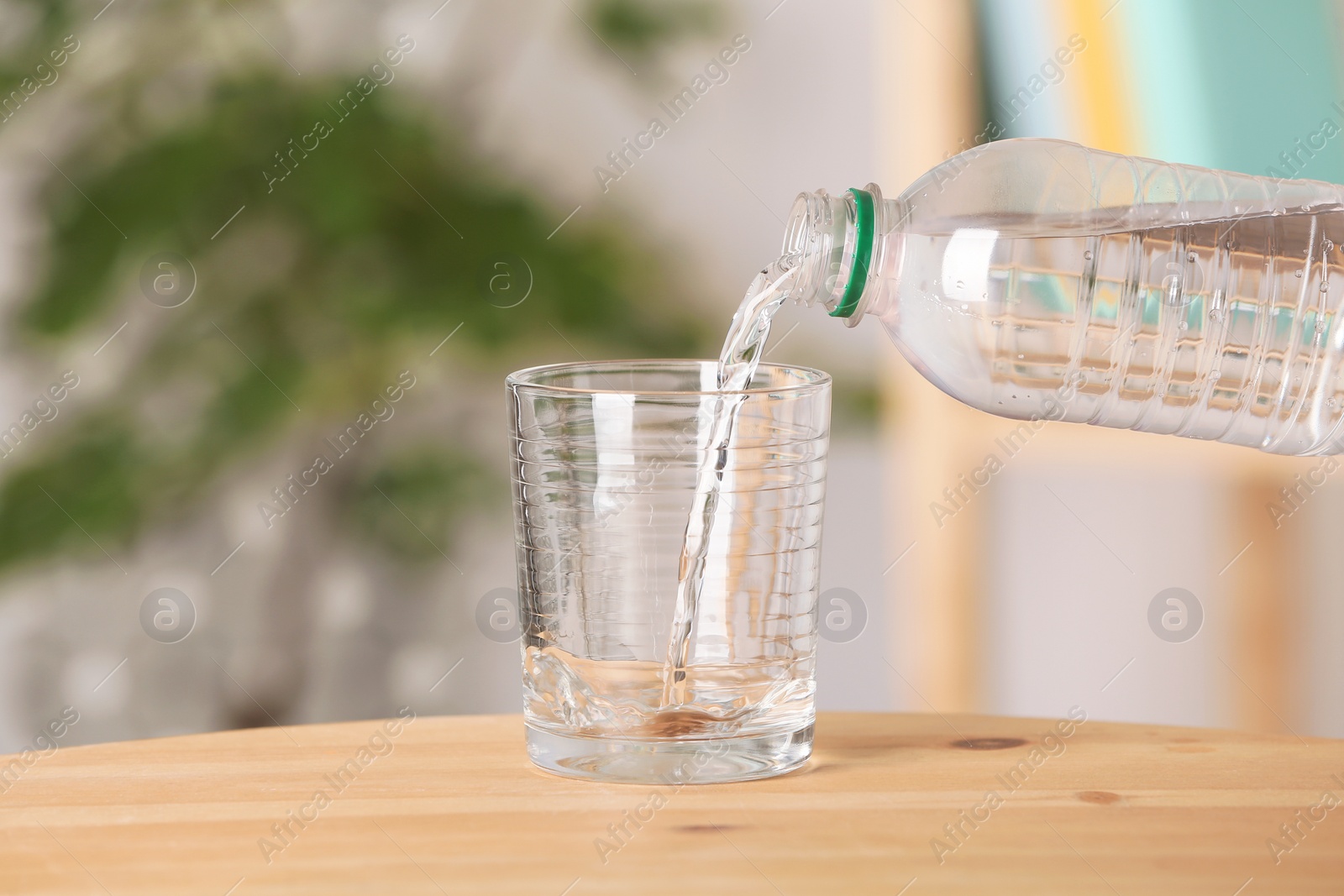Photo of Pouring water from bottle into glass on table against blurred background
