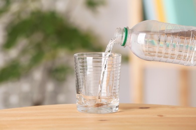 Pouring water from bottle into glass on table against blurred background