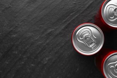 Energy drink in cans on black textured background, top view. Space for text