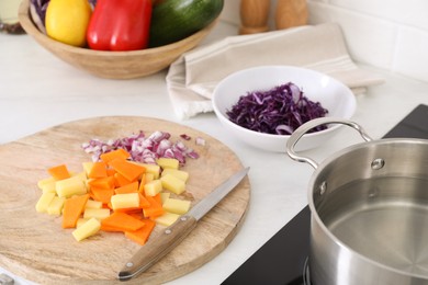 Photo of Board with cut vegetables and knife on white countertop in kitchen