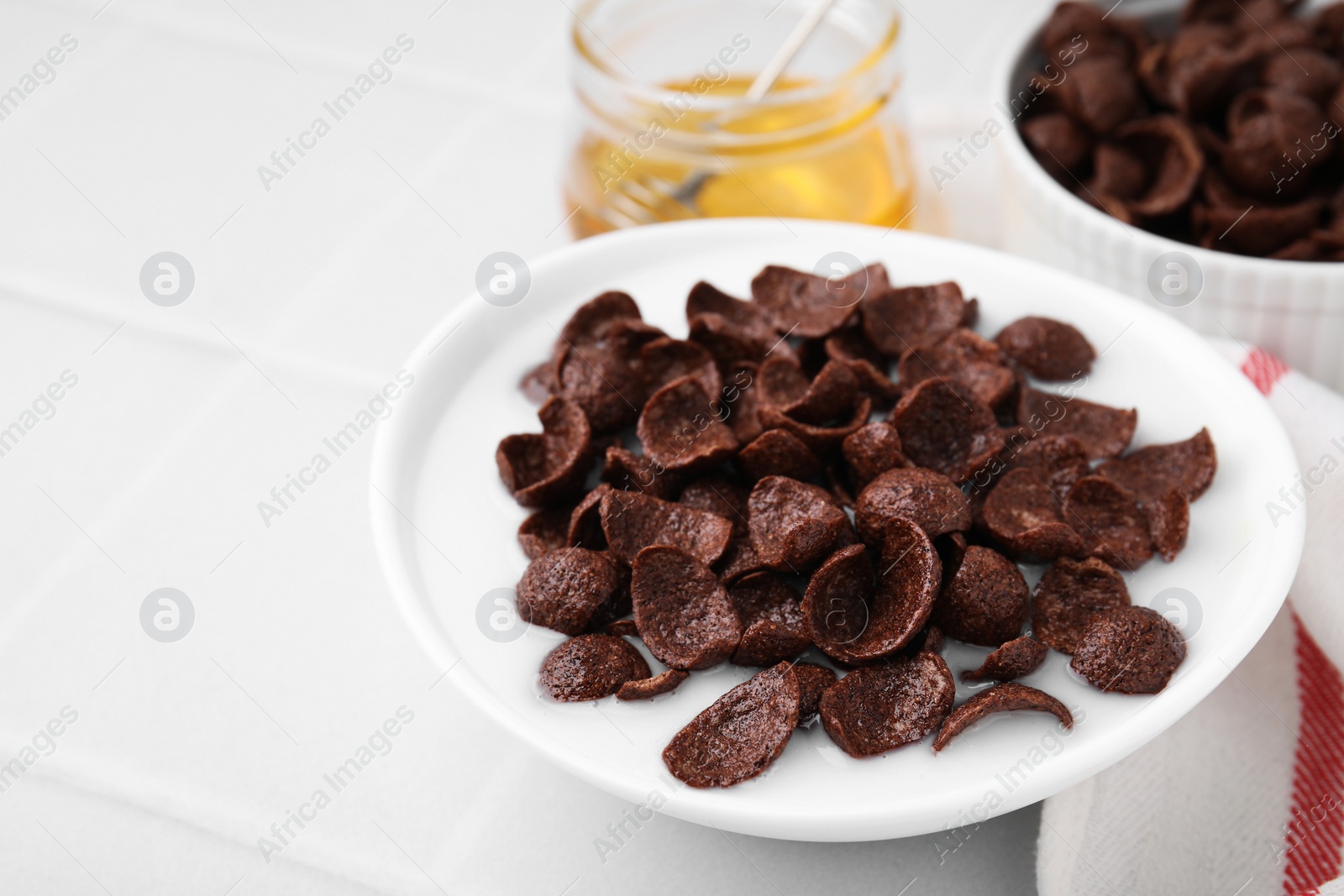 Photo of Breakfast cereal. Chocolate corn flakes and milk in bowl on white tiled table, closeup. Space for text