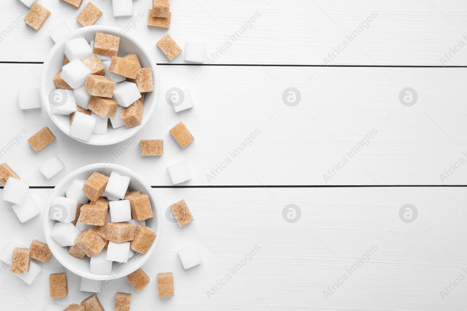 Photo of Different sugar cubes in bowls on white wooden table, flat lay. Space for text