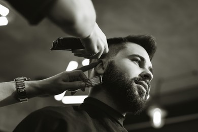 Image of Professional hairdresser working with client in barbershop, low angle view. Black and white effect