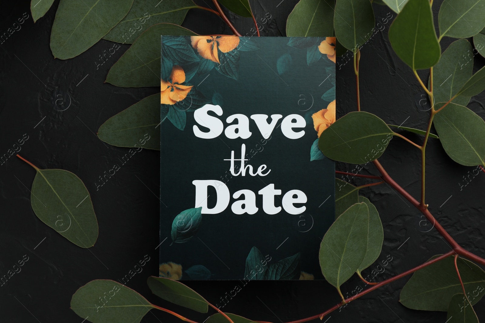 Photo of Beautiful card with Save the Date phrase and green leaves on black textured background, flat lay