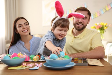 Photo of Happy family painting Easter eggs at table indoors
