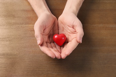 Photo of Man holding small red heart on wooden table. Heart attack concept