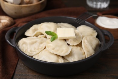 Photo of Serving pan of delicious dumplings (varenyky) with mushrooms on wooden table, closeup