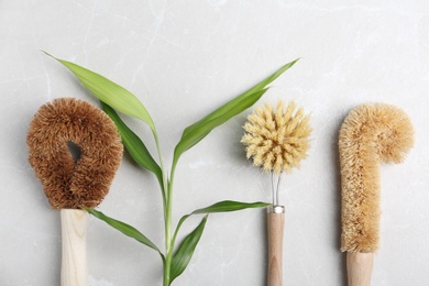 Photo of Cleaning brushes for dish washing and plant on grey table, flat lay