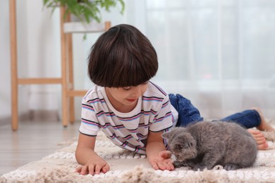 Photo of Cute little boy with kitten on floor at home. Childhood pet