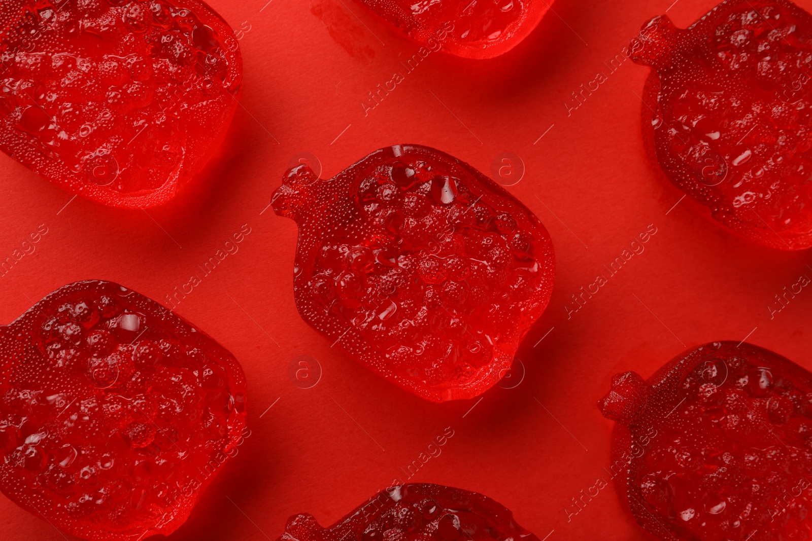 Photo of Delicious gummy pomegranate candies on red background, flat lay