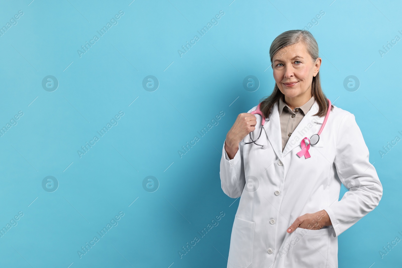 Photo of Mammologist with pink ribbon on light blue background, space for text. Breast cancer awareness