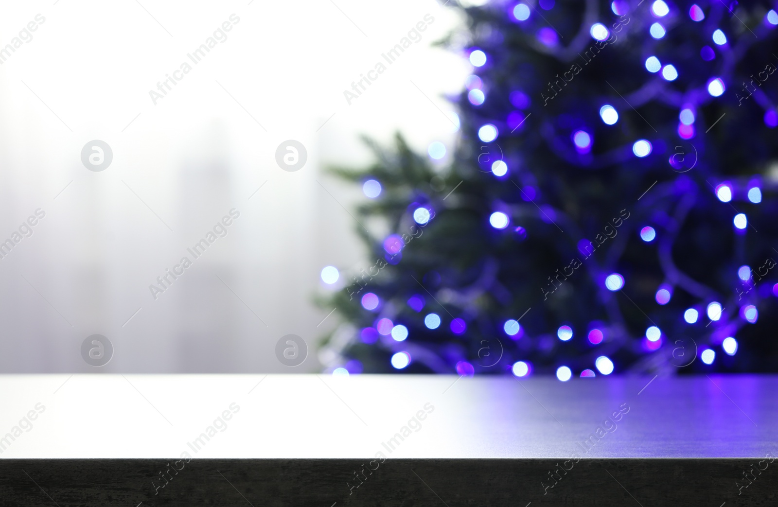 Photo of Empty table and blurred fir tree with violet Christmas lights on background, bokeh effect. Space for design