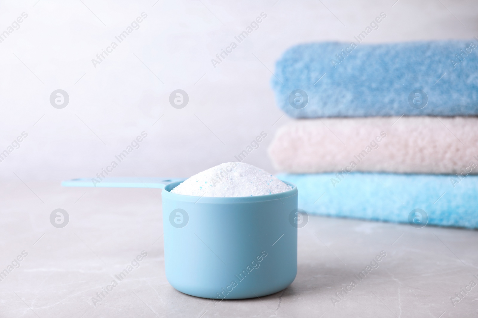 Photo of Measuring scoop of laundry powder and clean towels on marble table against light background