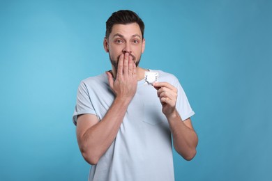 Photo of Confused man holding condom on light blue background