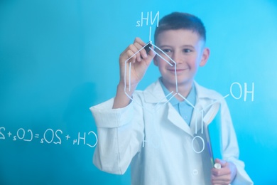 Schoolboy writing chemistry formula on glass board against color background. Space for text
