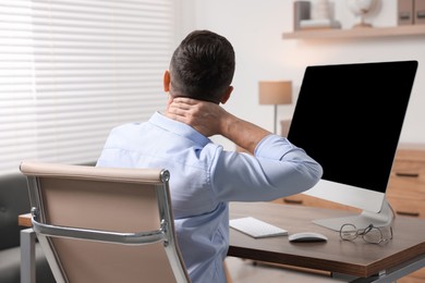 Photo of Man suffering from neck pain in office, back view
