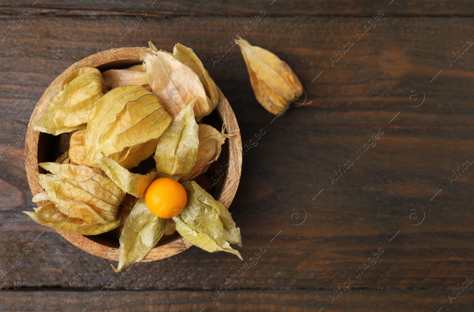 Photo of Ripe physalis fruits with calyxes in bowl on wooden table, top view. Space for text