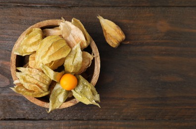 Ripe physalis fruits with calyxes in bowl on wooden table, top view. Space for text