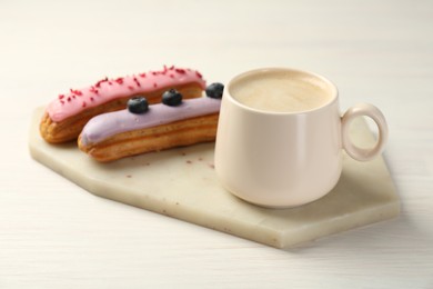 Photo of Cup of coffee and delicious eclairs covered with glaze on white wooden table