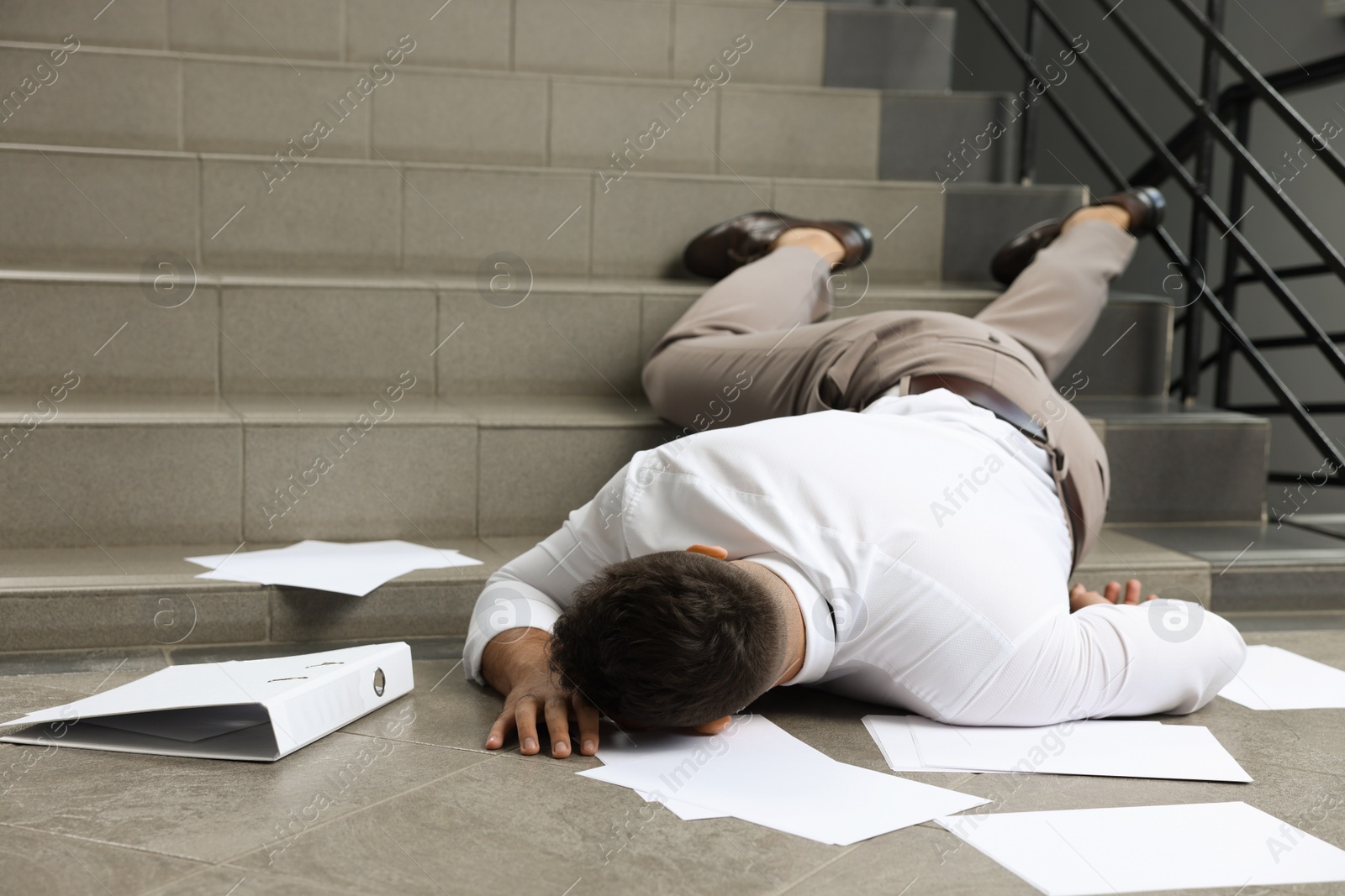 Photo of Unconscious man with scattered folder and papers lying on floor after falling down stairs indoors