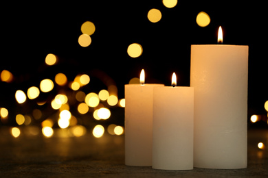 Photo of Burning candles on table against festive lights, space for text. Bokeh effect
