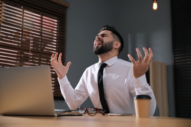 Photo of Emotional young businessman working on laptop in office. Online hate concept