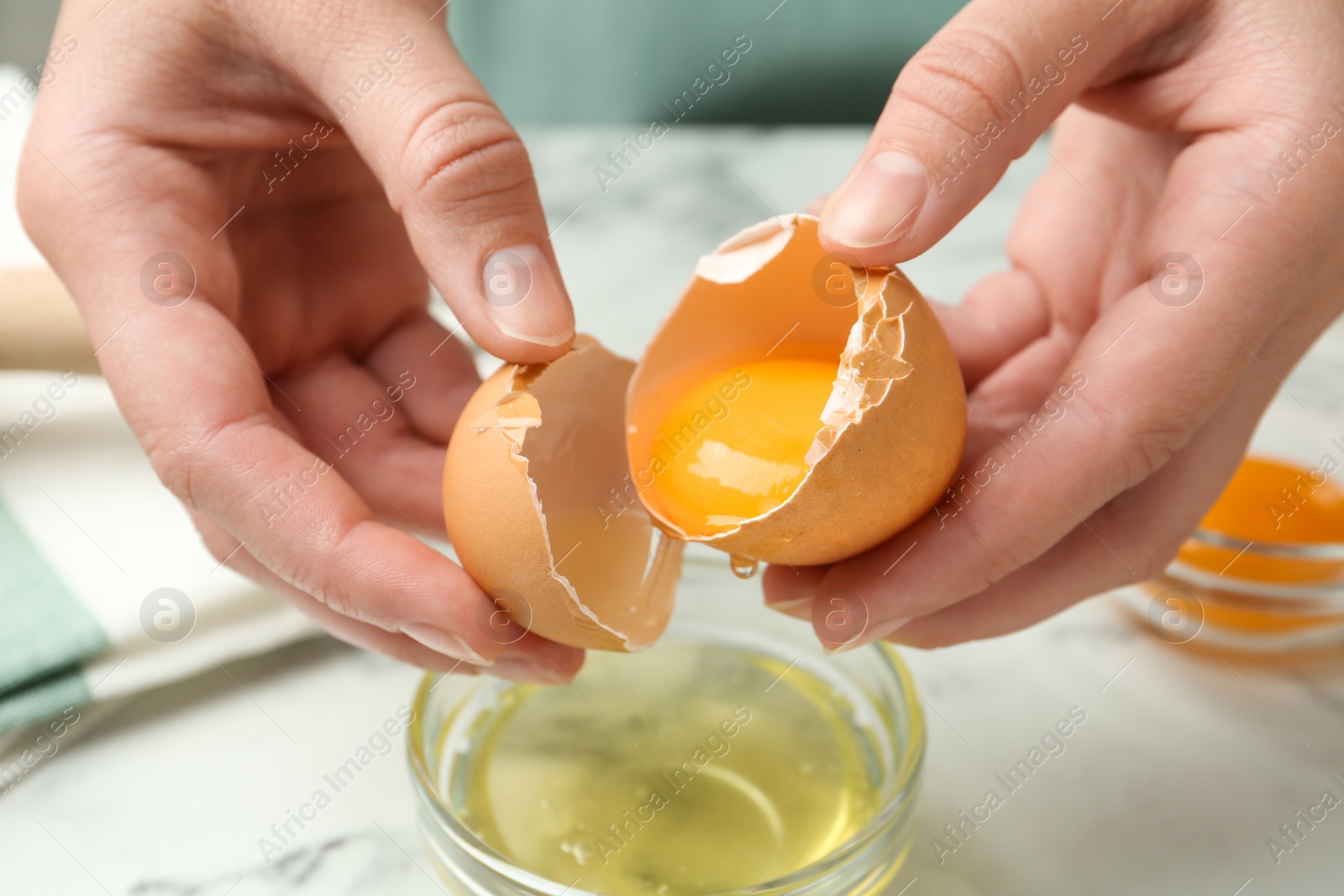 Photo of Woman separating egg yolk from white over glass bowl at table, closeup