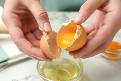 Photo of Woman separating egg yolk from white over glass bowl at table, closeup