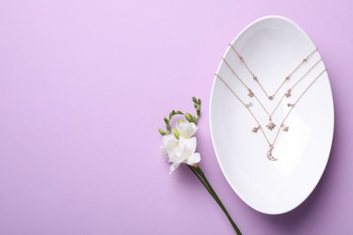 Photo of Beautiful jewelry and freesia flower on pale violet background, flat lay. Space for text