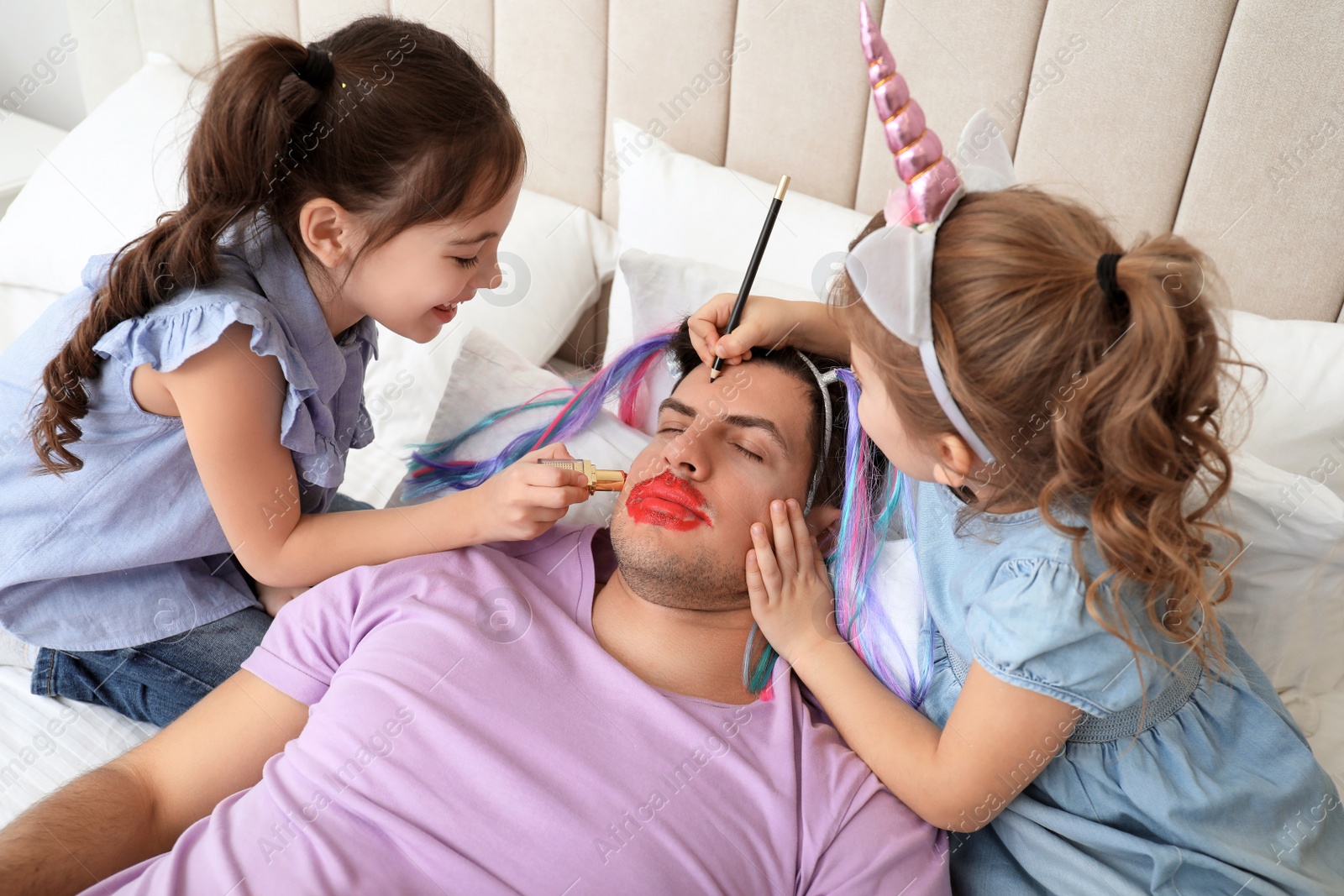 Photo of Cute little children painting face of their father while he sleeping in bed at home