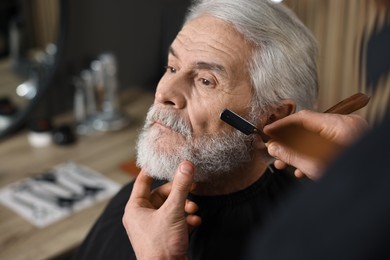 Photo of Professional barber shaving client's beard with blade in barbershop, space for text