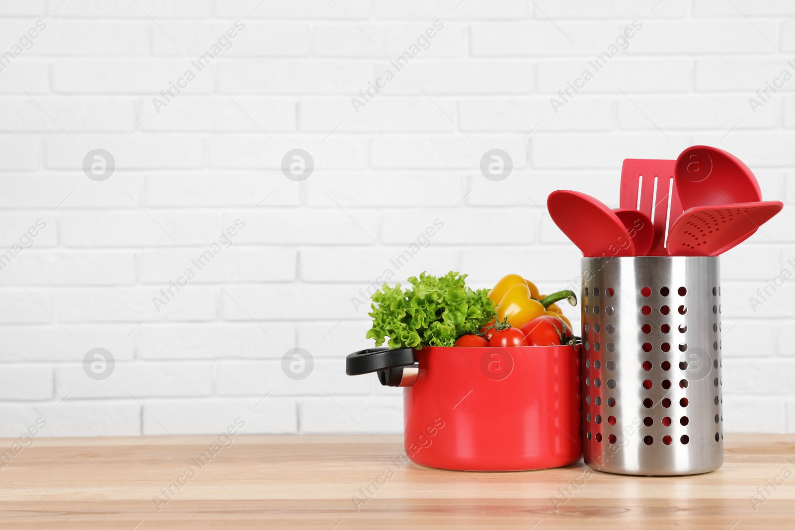 Photo of Set of clean cookware, utensils and vegetables on table against white brick wall. Space for text