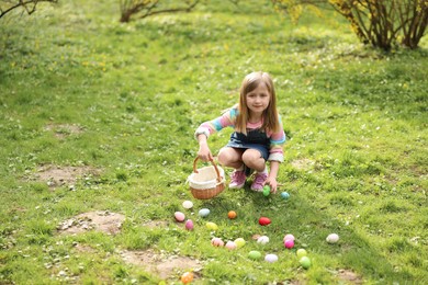 Photo of Easter celebration. Cute little girl hunting eggs outdoors