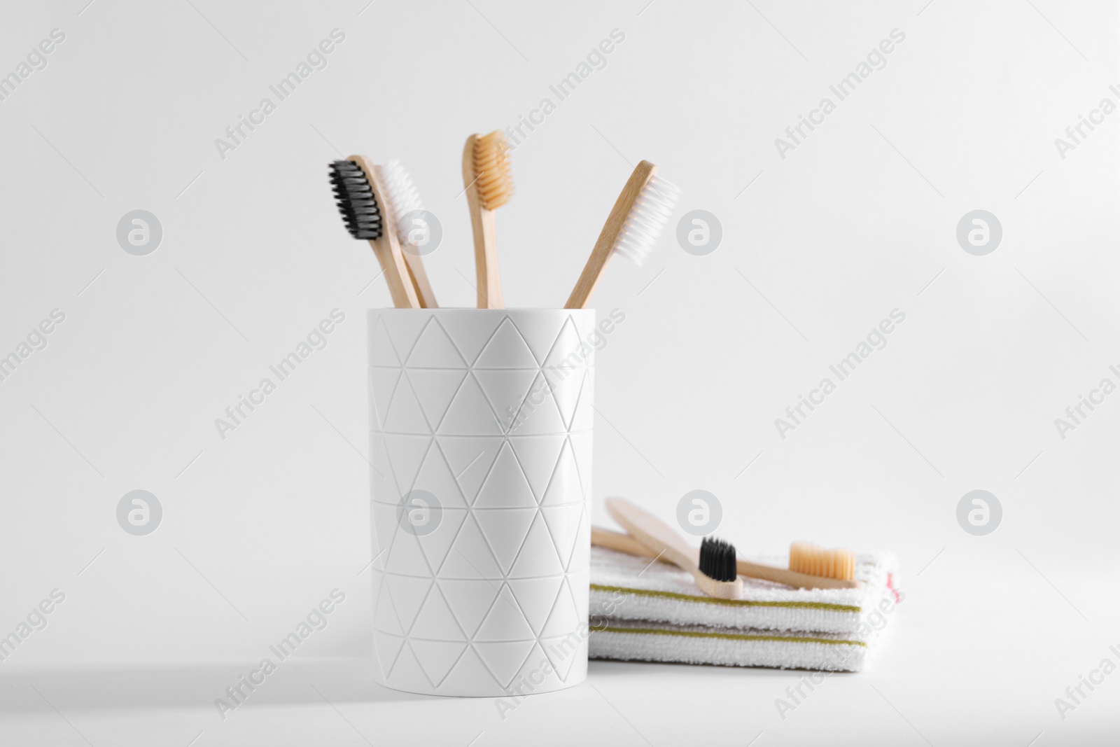 Photo of Bamboo toothbrushes in holder and towel on white background