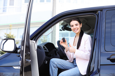 Photo of Young woman with key sitting in car outdoors. Buying new auto