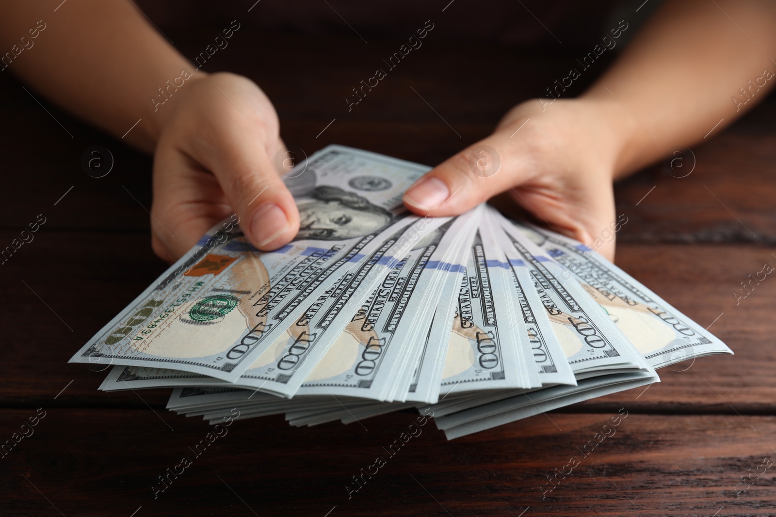 Photo of Woman holding dollar banknotes at wooden table, closeup