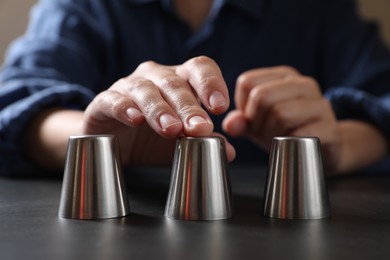 Photo of Woman playing thimblerig game with metal cups at black table, closeup