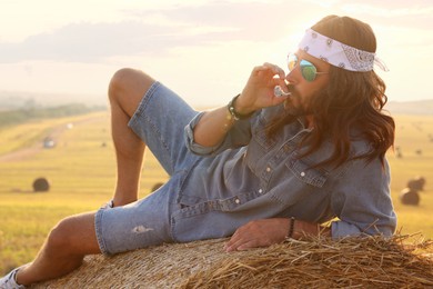 Hippie man smoking joint on hay bale in field