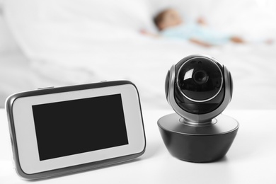 Photo of Baby monitor and camera on table near bed with child in room. Video nanny