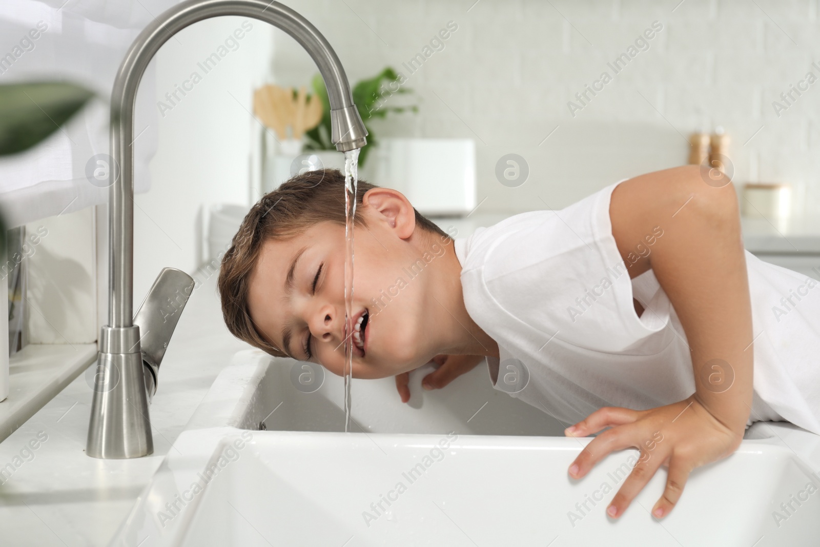 Photo of Boy drinking tap water over sink in kitchen