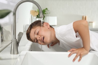 Photo of Boy drinking tap water over sink in kitchen
