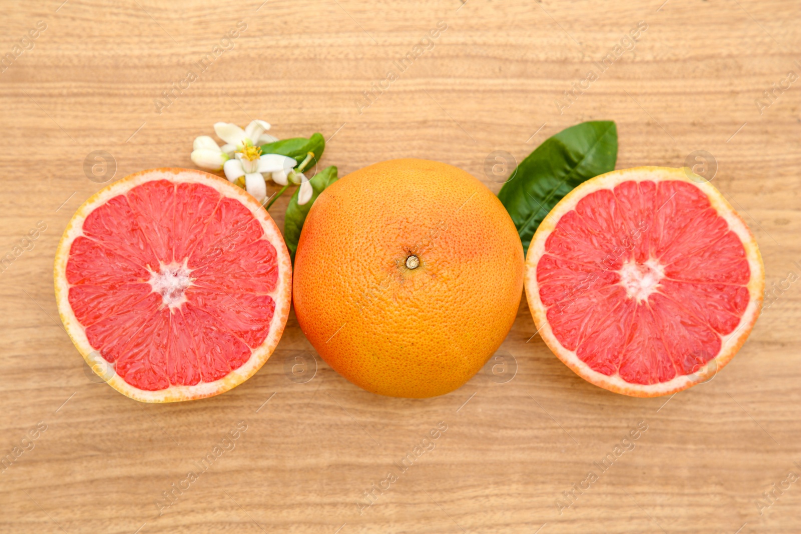 Photo of Fresh ripe grapefruits, flowers and green leaves on wooden table, flat lay