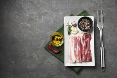 Photo of Pieces of raw pork belly, oil, peppercorns, rosemary and garlic on grey textured table, flat lay. Space for text