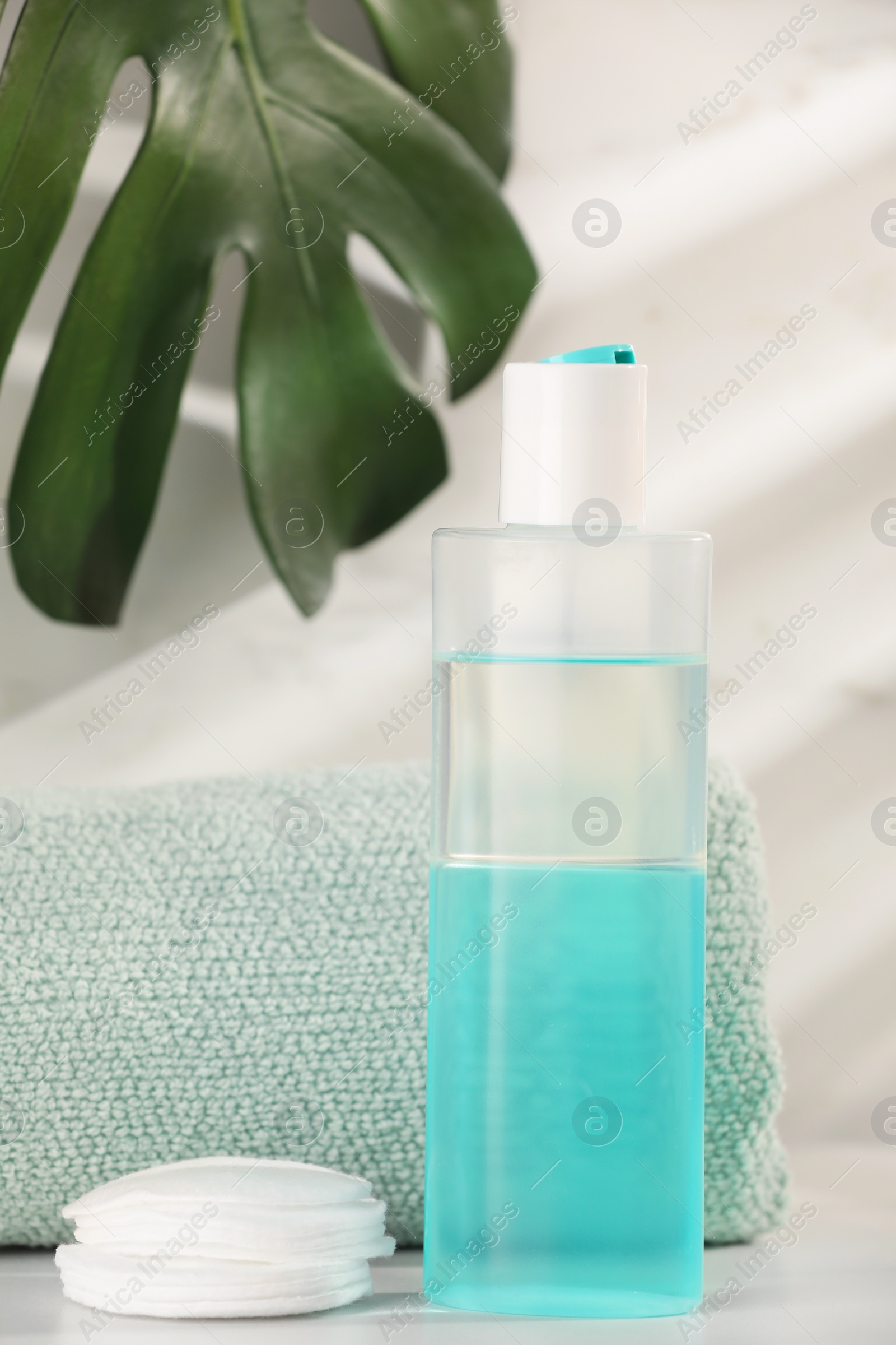 Photo of Bottle of micellar water, towel and cotton pads on white table against marble background