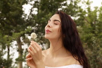 Photo of Beautiful young woman blowing dandelion in park. Allergy free concept