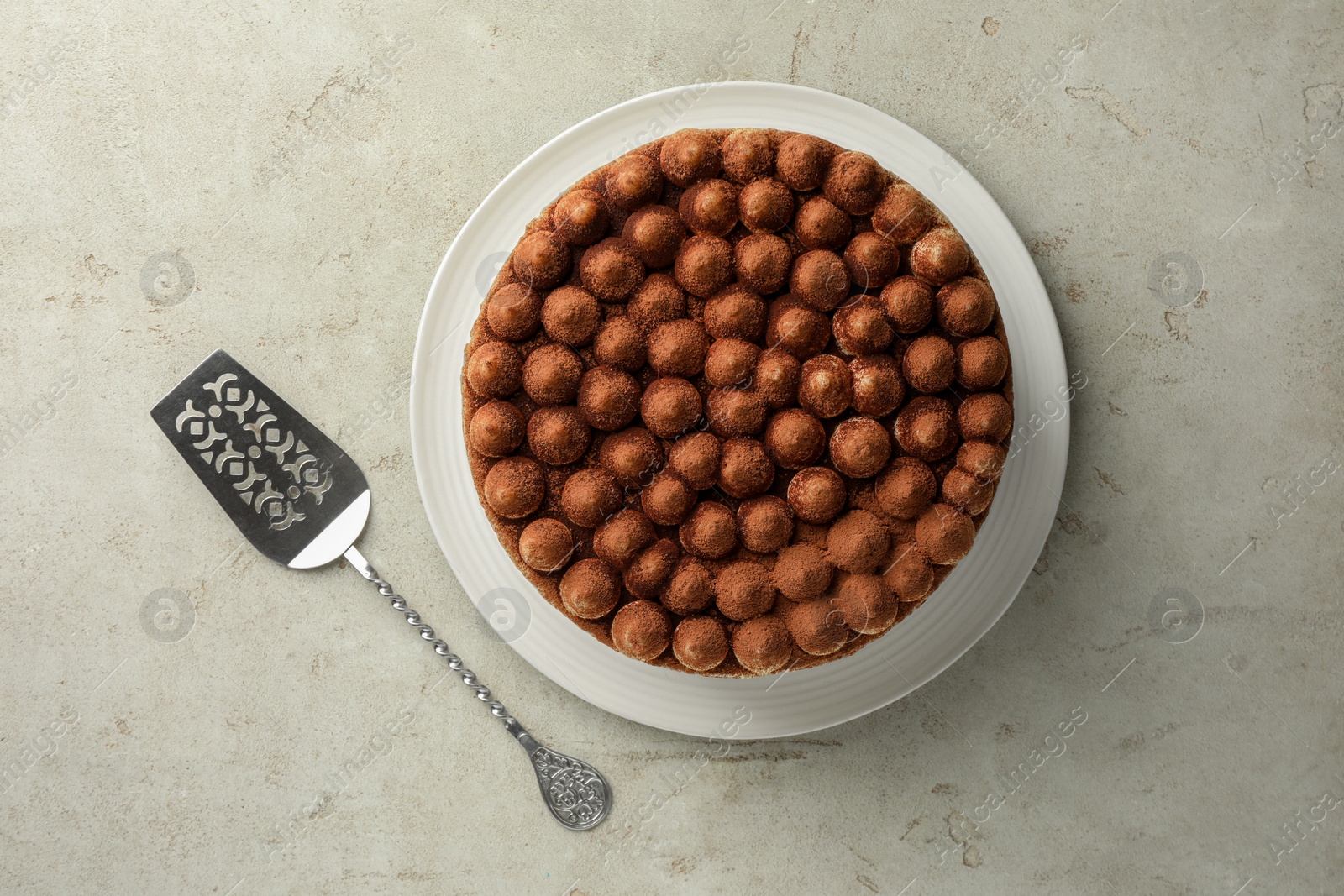 Photo of Delicious tiramisu cake with cocoa powder and server on light grey textured table, flat lay